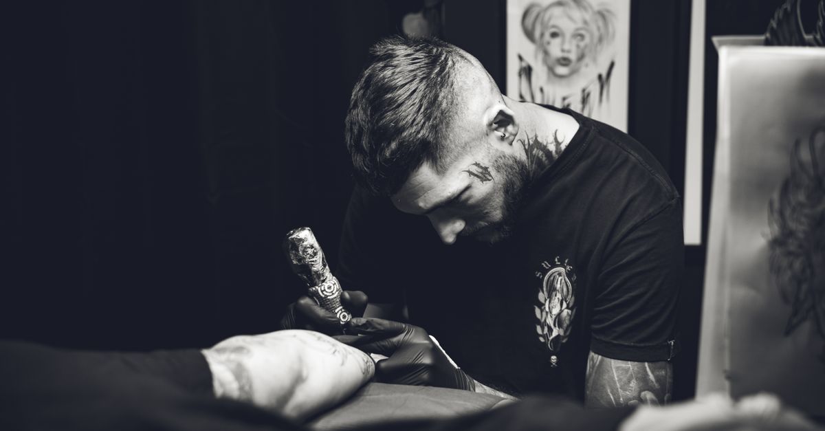 Black and white photo of a focused tattoo artist working in a studio, capturing the art of inking.